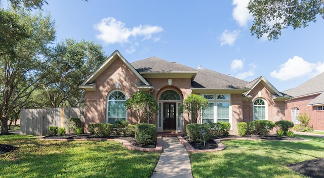 view of front of home with brick siding, roof with shingles, fence, and a front yard