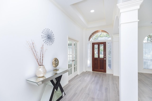 foyer entrance with wood finished floors, french doors, ornate columns, a raised ceiling, and crown molding