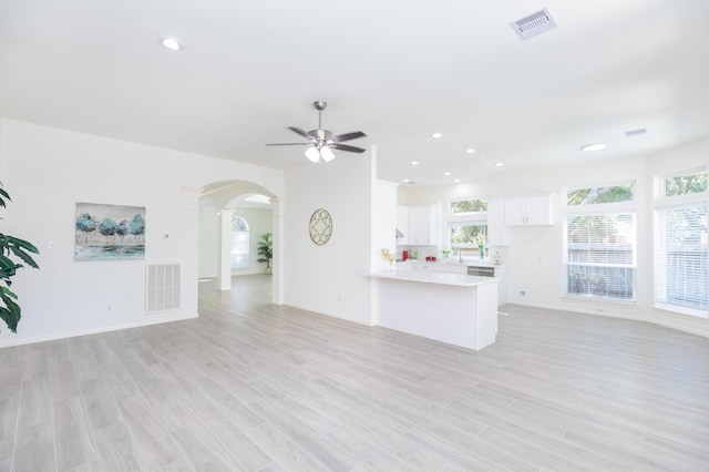 unfurnished living room with a wealth of natural light, visible vents, arched walkways, and light wood finished floors