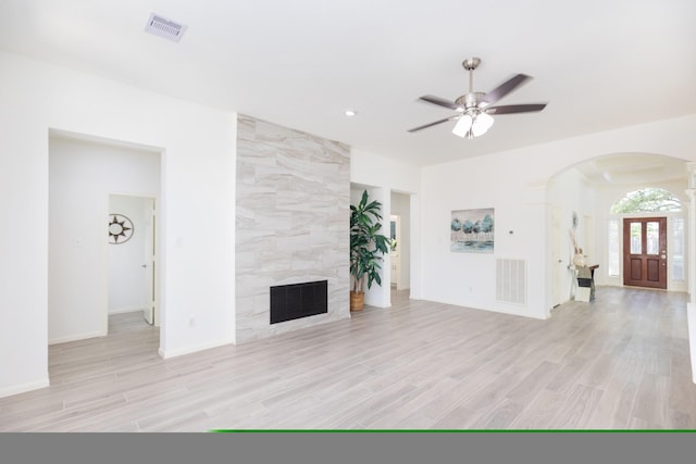 unfurnished living room with arched walkways, light wood finished floors, a fireplace, and visible vents