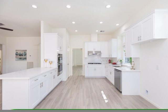 kitchen with under cabinet range hood, stainless steel appliances, a peninsula, a sink, and tasteful backsplash