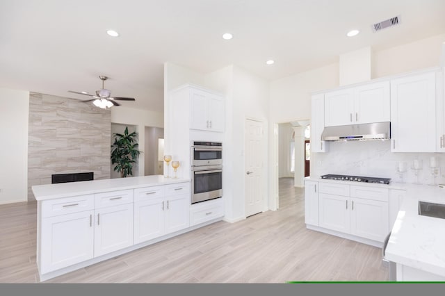 kitchen featuring tasteful backsplash, stainless steel double oven, white cabinets, gas cooktop, and under cabinet range hood