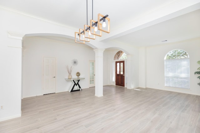 foyer with ornamental molding, arched walkways, ornate columns, and light wood finished floors