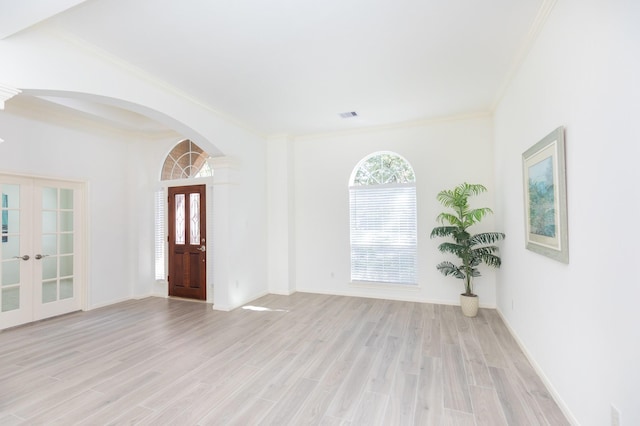 entrance foyer featuring light wood finished floors, arched walkways, ornamental molding, and french doors