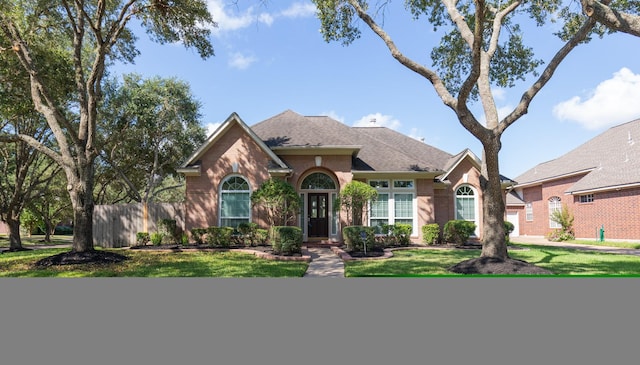 view of front of property featuring a shingled roof, fence, a front lawn, and brick siding