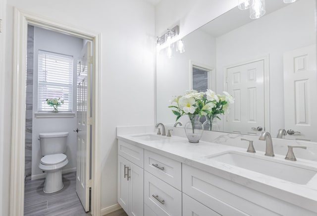 full bath with double vanity, a sink, toilet, and baseboards