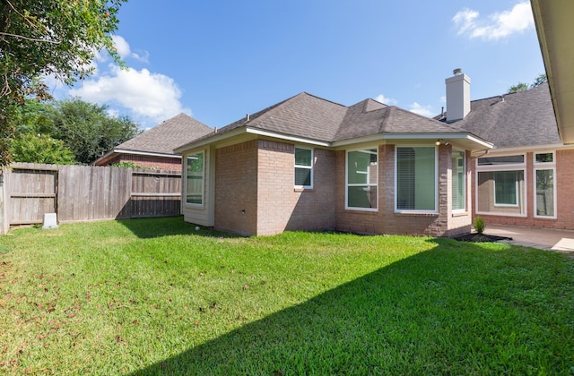 back of house with a chimney, brick siding, a lawn, and a fenced backyard