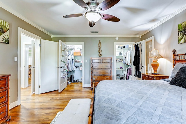 bedroom with visible vents, baseboards, light wood-style floors, ornamental molding, and a walk in closet