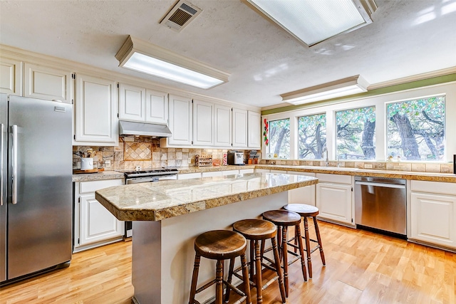 kitchen with under cabinet range hood, a kitchen island, visible vents, appliances with stainless steel finishes, and tile counters