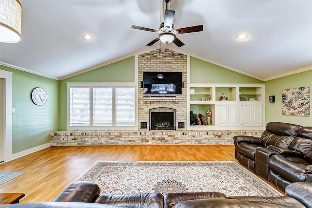 living room with ceiling fan, ornamental molding, wood finished floors, vaulted ceiling, and a brick fireplace