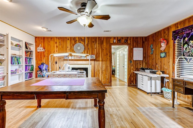 living room with wooden walls, visible vents, ceiling fan, wood finished floors, and built in shelves