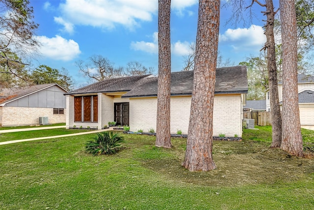 view of front of house featuring central AC, a front lawn, roof with shingles, and brick siding