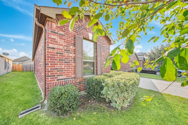 view of property exterior with brick siding, a lawn, and fence