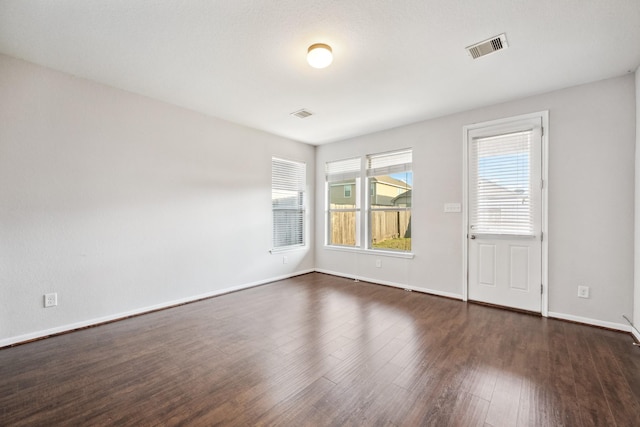 unfurnished room with visible vents, dark wood finished floors, and baseboards