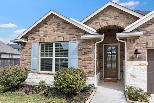 view of exterior entry with fence and brick siding