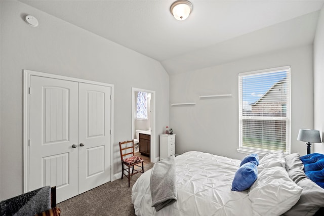 bedroom featuring lofted ceiling, dark colored carpet, a closet, and ensuite bathroom