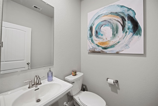 half bathroom with visible vents, a textured wall, a sink, and toilet