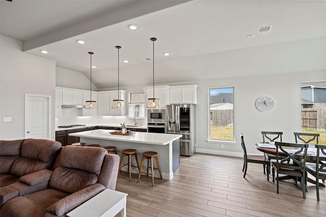 kitchen with open floor plan, light countertops, stainless steel appliances, light wood-type flooring, and backsplash