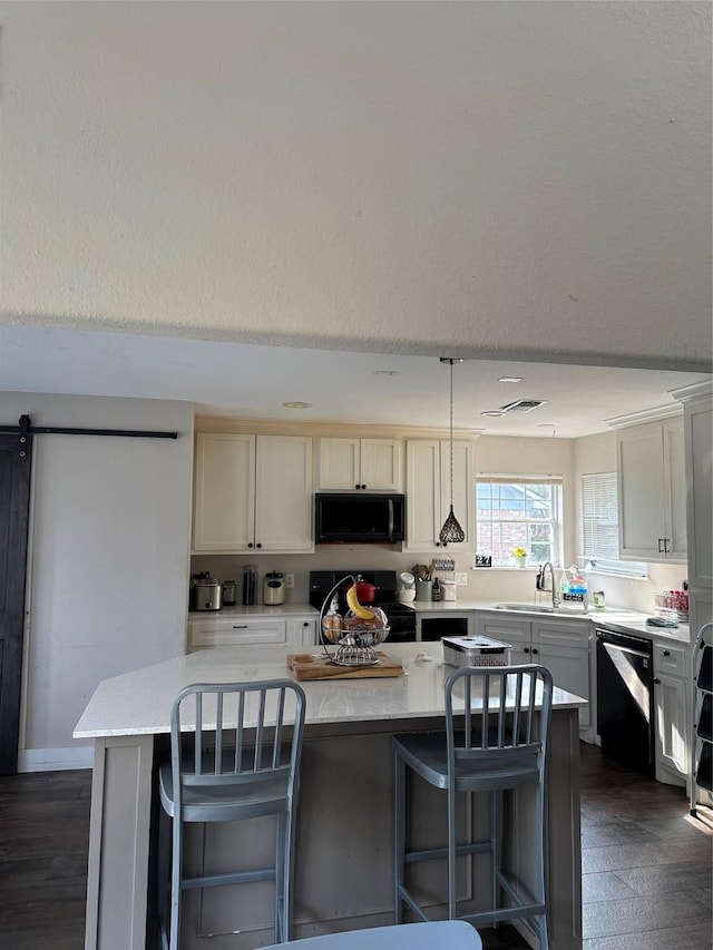 kitchen featuring a breakfast bar area, a sink, hanging light fixtures, a center island, and black appliances