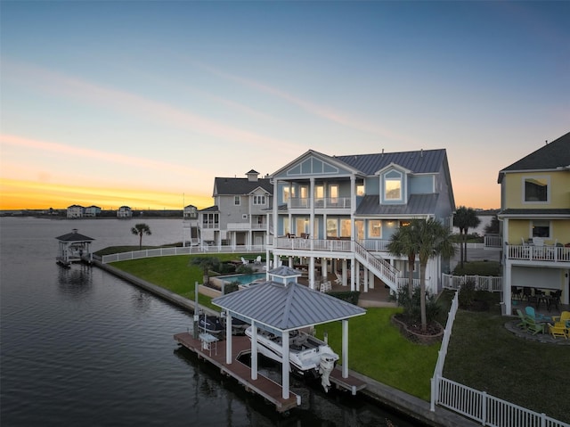 rear view of property featuring a lawn, a water view, boat lift, and a balcony