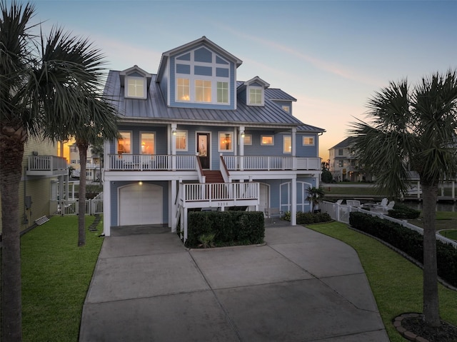 coastal home with an attached garage, covered porch, concrete driveway, a front lawn, and a standing seam roof