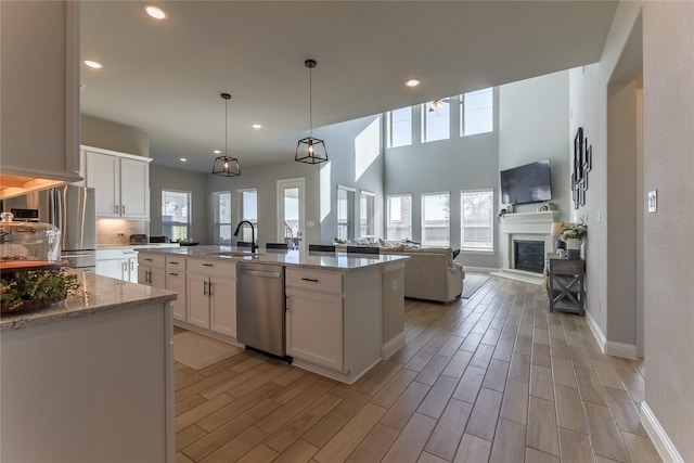 kitchen featuring wood finish floors, white cabinetry, open floor plan, appliances with stainless steel finishes, and a glass covered fireplace