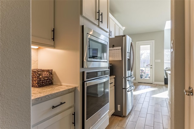 kitchen featuring light stone countertops, white cabinetry, baseboards, appliances with stainless steel finishes, and wood tiled floor