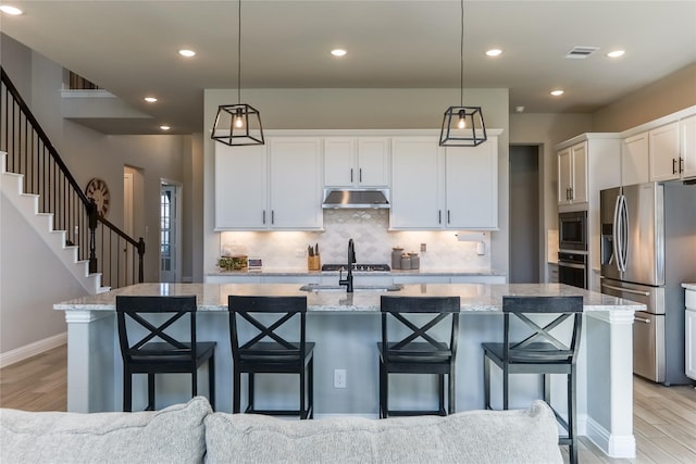 kitchen with under cabinet range hood, visible vents, appliances with stainless steel finishes, and light wood-style floors