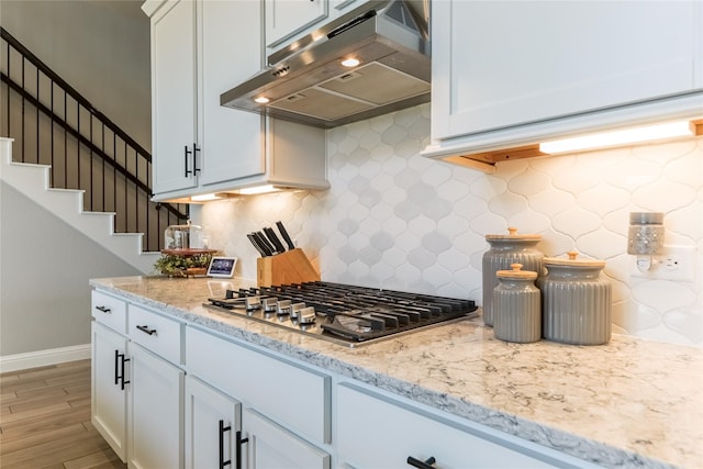 kitchen with light stone counters, stainless steel gas cooktop, backsplash, light wood-type flooring, and under cabinet range hood