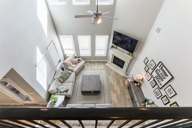 unfurnished living room featuring visible vents, a towering ceiling, a ceiling fan, a glass covered fireplace, and wood finished floors