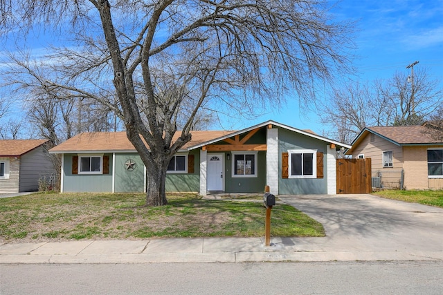 view of front facade with brick siding, driveway, a front lawn, and fence