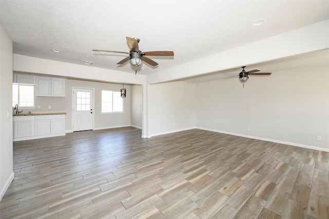 unfurnished living room featuring a ceiling fan, baseboards, visible vents, and light wood finished floors