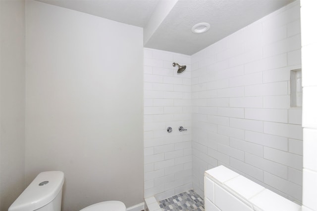 bathroom with a textured ceiling, a tile shower, and toilet