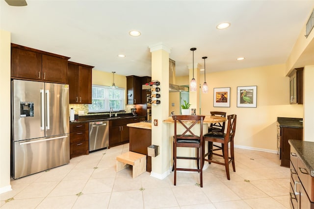 kitchen featuring stainless steel appliances, wall chimney range hood, dark brown cabinets, and tasteful backsplash