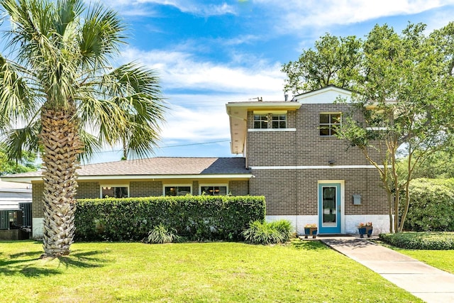 view of front of house with brick siding, a front lawn, and roof with shingles