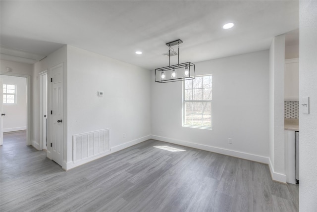 unfurnished dining area with light wood-type flooring, a healthy amount of sunlight, visible vents, and baseboards