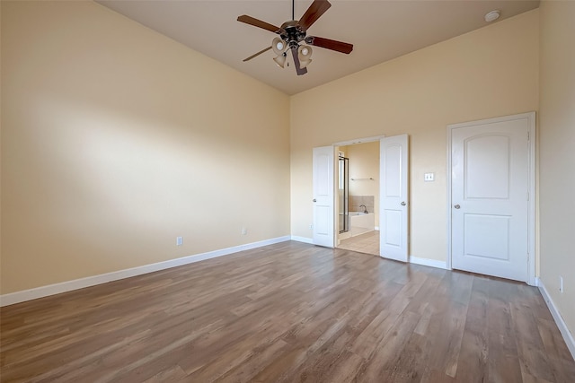 unfurnished bedroom featuring baseboards, ensuite bath, a high ceiling, and wood finished floors