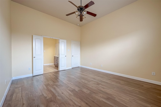 unfurnished bedroom with a high ceiling, wood finished floors, baseboards, and connected bathroom