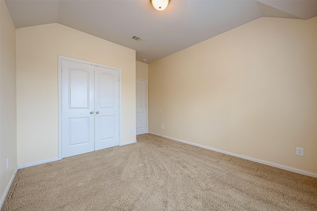 unfurnished bedroom with visible vents, light carpet, lofted ceiling, a closet, and baseboards