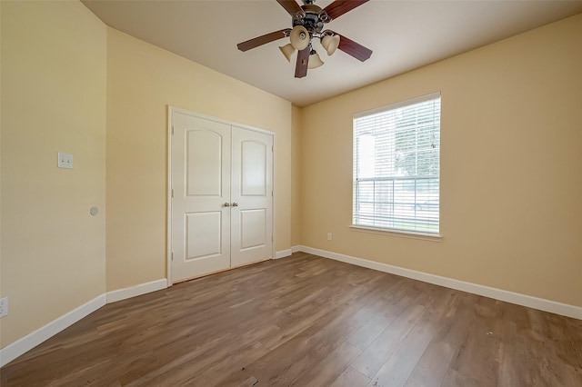 unfurnished bedroom with a closet, a ceiling fan, baseboards, and wood finished floors