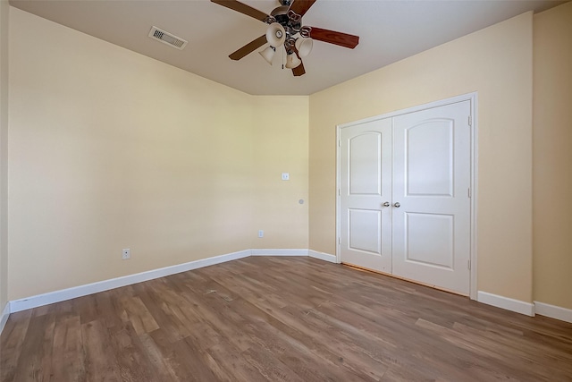 unfurnished bedroom featuring wood finished floors, visible vents, a closet, and baseboards