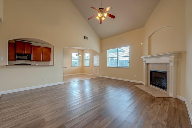 unfurnished living room with high vaulted ceiling, a tiled fireplace, light wood-style floors, baseboards, and ceiling fan