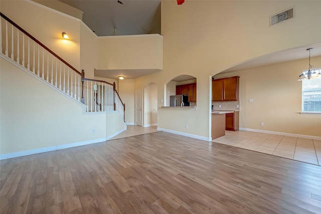 unfurnished living room with stairway, light wood-style flooring, visible vents, and baseboards