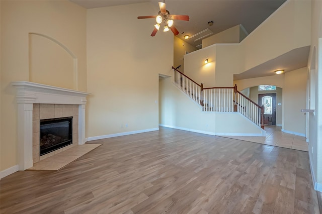 unfurnished living room featuring baseboards, stairs, a tile fireplace, a towering ceiling, and wood finished floors