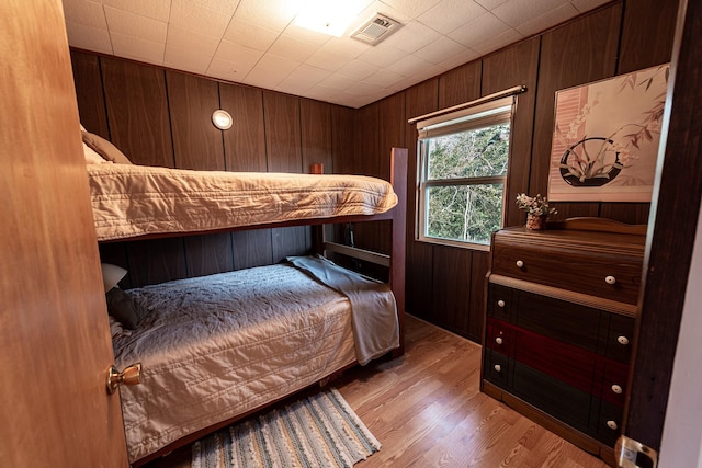 bedroom featuring visible vents, wood walls, and wood finished floors