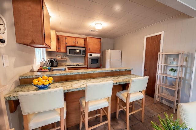 kitchen with stainless steel appliances, brown cabinetry, a sink, a peninsula, and a kitchen bar