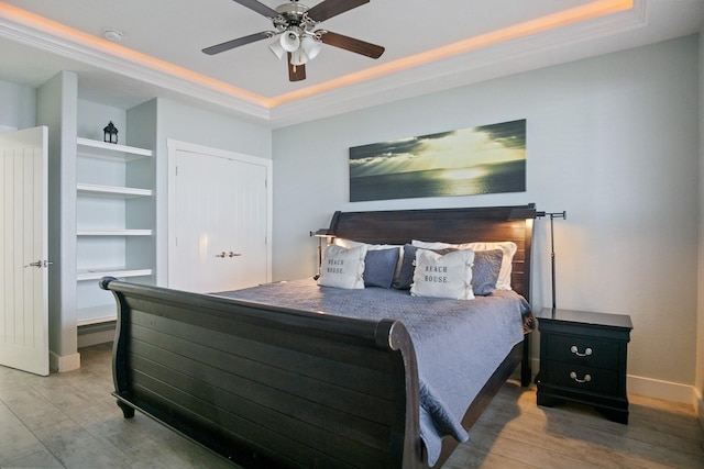 bedroom featuring ceiling fan, a tray ceiling, wood finished floors, and baseboards