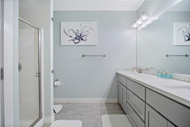 full bath with double vanity, baseboards, crown molding, a shower stall, and a sink