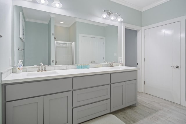 full bathroom featuring double vanity, a stall shower, wood finished floors, crown molding, and a sink