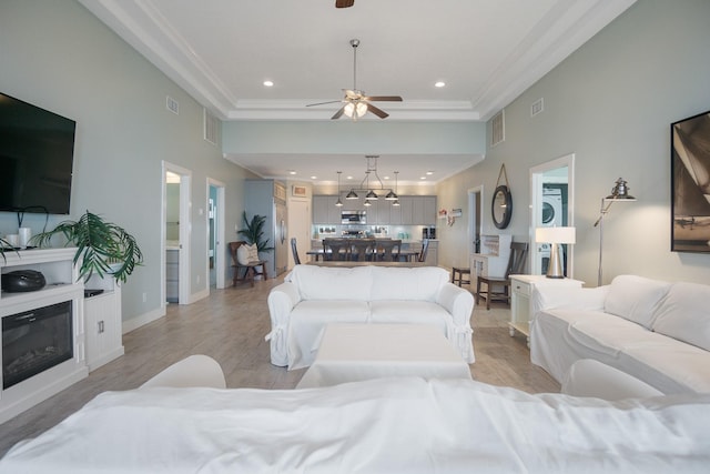 living room featuring light wood-style flooring, recessed lighting, visible vents, ornamental molding, and a glass covered fireplace